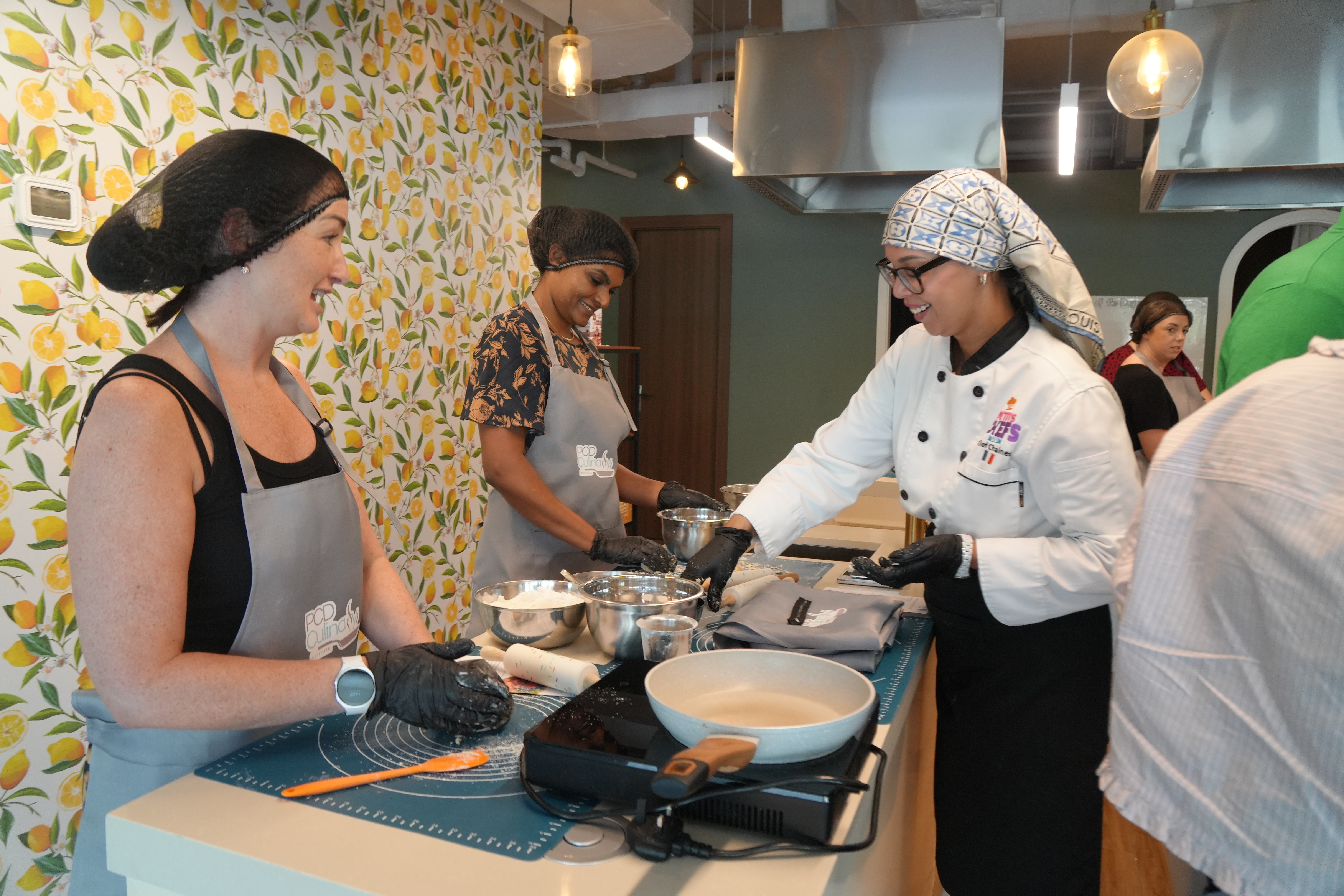 A PCD chef-instructor guiding two participants through pastry work at a workstation